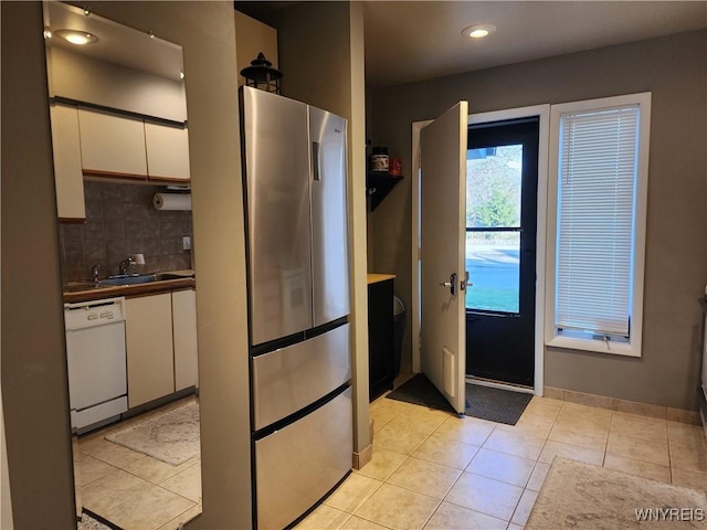 kitchen with dishwasher, white cabinets, sink, light tile patterned floors, and stainless steel refrigerator