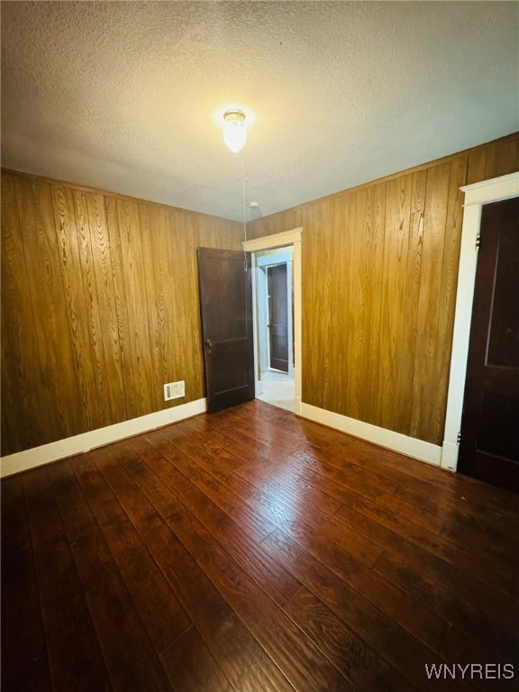 empty room featuring wood walls, dark hardwood / wood-style flooring, and a textured ceiling