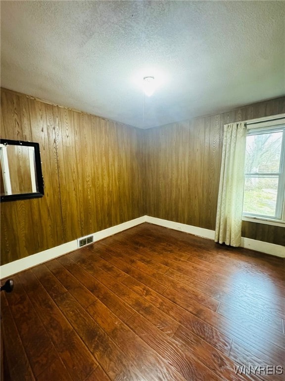 unfurnished room with dark hardwood / wood-style floors, wood walls, and a textured ceiling