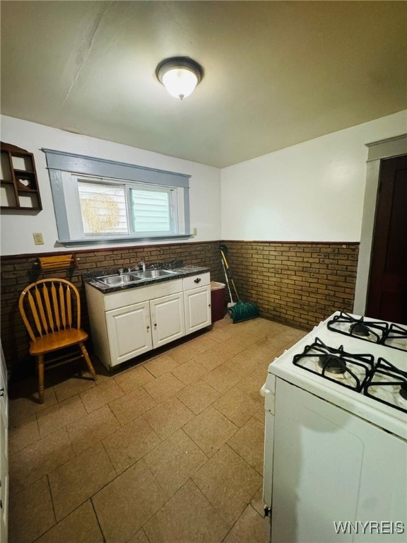 kitchen featuring white cabinetry, sink, white range with gas stovetop, and brick wall