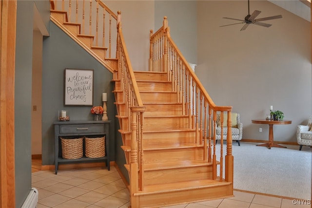 stairs featuring tile patterned flooring, a towering ceiling, baseboard heating, and ceiling fan