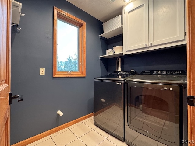 clothes washing area with washer and clothes dryer, light tile patterned flooring, cabinets, and a textured ceiling