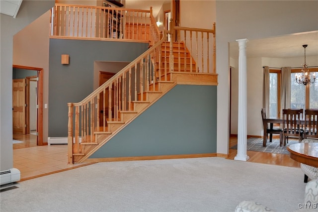 staircase with a towering ceiling, ornate columns, hardwood / wood-style flooring, a baseboard radiator, and a chandelier