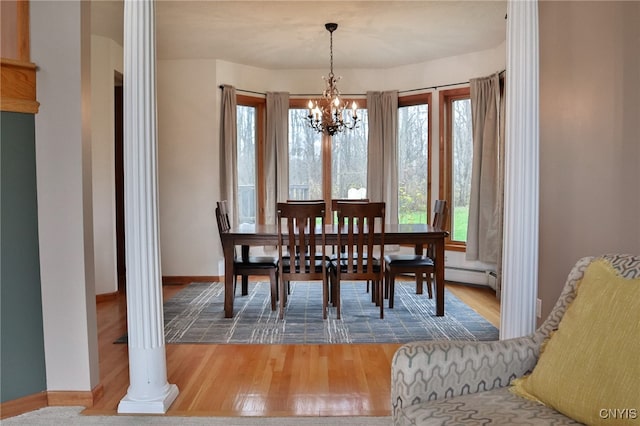 dining area with ornate columns, hardwood / wood-style flooring, a baseboard heating unit, and an inviting chandelier