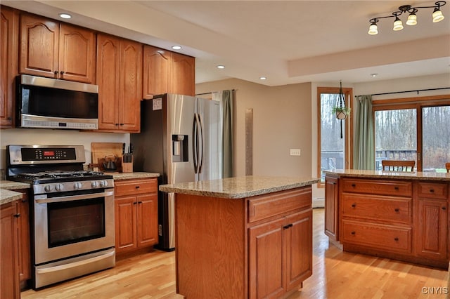 kitchen featuring a kitchen island, light stone counters, light wood-type flooring, and stainless steel appliances