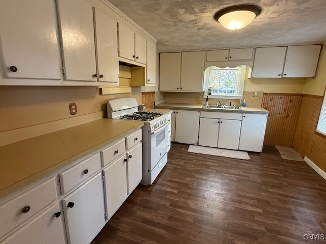 kitchen featuring white gas range, dark wood-type flooring, wooden walls, sink, and white cabinetry