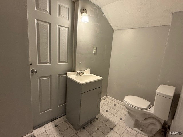 bathroom with toilet, vanity, vaulted ceiling, and tile patterned flooring