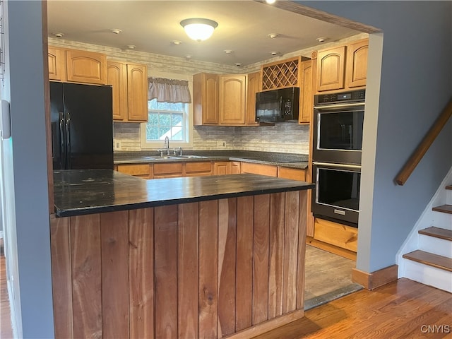 kitchen featuring sink, kitchen peninsula, hardwood / wood-style floors, decorative backsplash, and black appliances