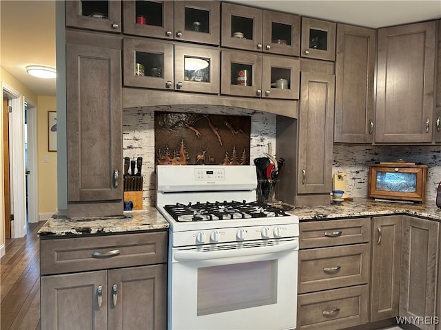 kitchen with backsplash, dark wood-type flooring, white gas range oven, light stone countertops, and dark brown cabinetry