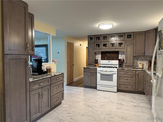 kitchen featuring decorative backsplash, gas range gas stove, dark brown cabinetry, and light stone counters