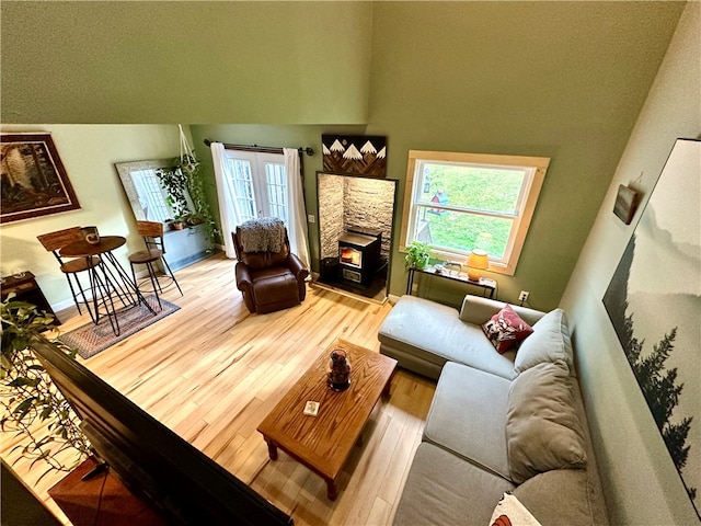 living room with a stone fireplace, wood-type flooring, and a towering ceiling