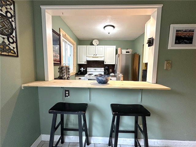 kitchen with backsplash, a kitchen breakfast bar, electric range, stainless steel fridge, and white cabinetry