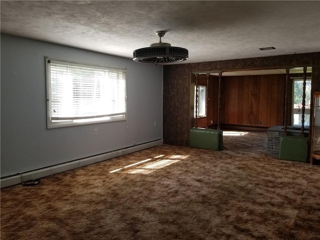 empty room with a baseboard heating unit, visible vents, carpet floors, and a textured ceiling