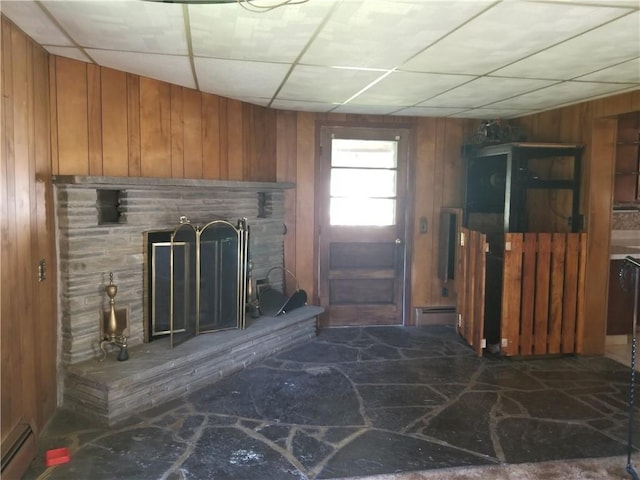 unfurnished living room featuring a fireplace with raised hearth, baseboard heating, a paneled ceiling, and wooden walls