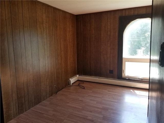 unfurnished room with baseboard heating, wood walls, plenty of natural light, and wood finished floors