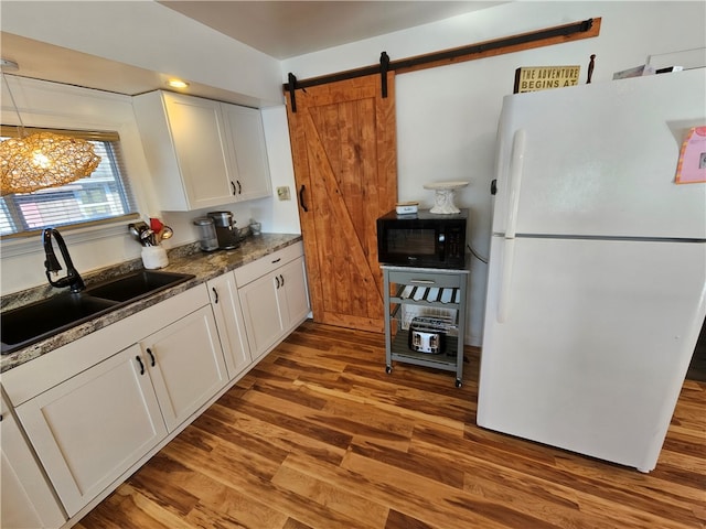 kitchen with sink, white refrigerator, a barn door, white cabinets, and light hardwood / wood-style floors