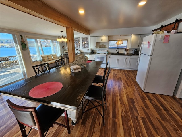 dining area with sink, a barn door, dark hardwood / wood-style floors, a chandelier, and a water view