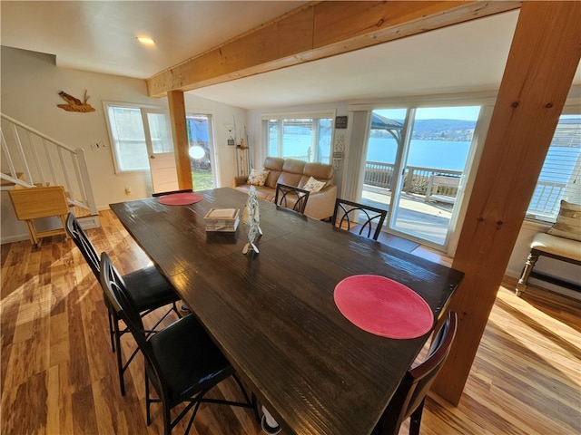 dining area with lofted ceiling with beams, a water view, and light hardwood / wood-style flooring