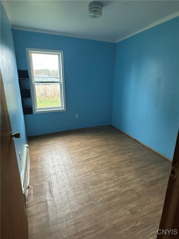 spare room featuring hardwood / wood-style floors, a baseboard radiator, and ornamental molding