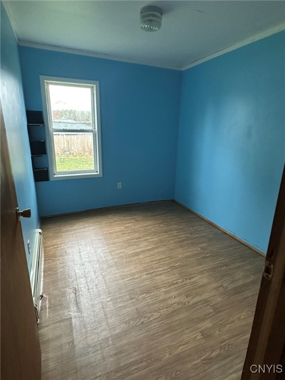 empty room with hardwood / wood-style floors, ornamental molding, and a baseboard heating unit