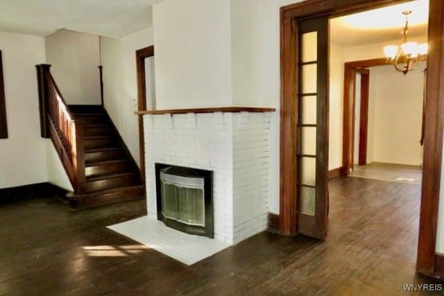 unfurnished living room featuring a chandelier, a fireplace, and dark wood-type flooring