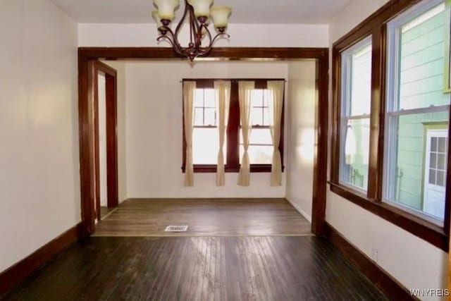 unfurnished room featuring a notable chandelier and dark hardwood / wood-style flooring