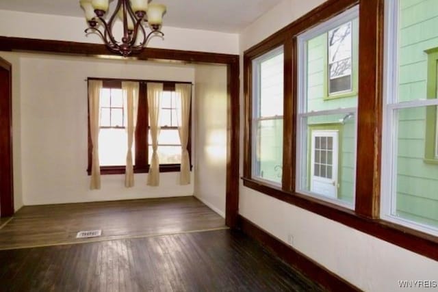 spare room with a notable chandelier and dark wood-type flooring