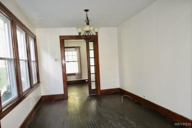 spare room featuring a wealth of natural light, dark hardwood / wood-style flooring, and a chandelier