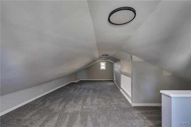 additional living space with dark colored carpet and vaulted ceiling