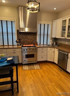 kitchen with light wood-type flooring, stainless steel appliances, exhaust hood, decorative light fixtures, and white cabinetry