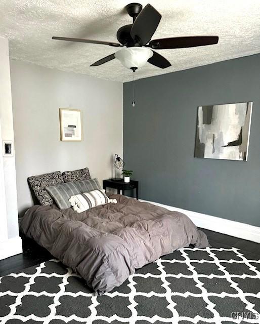 bedroom with dark wood-type flooring, a textured ceiling, and ceiling fan