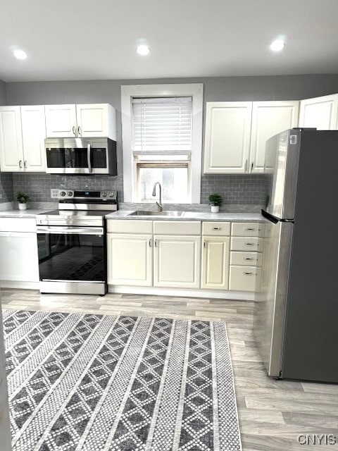 kitchen with appliances with stainless steel finishes, tasteful backsplash, white cabinetry, sink, and light hardwood / wood-style flooring