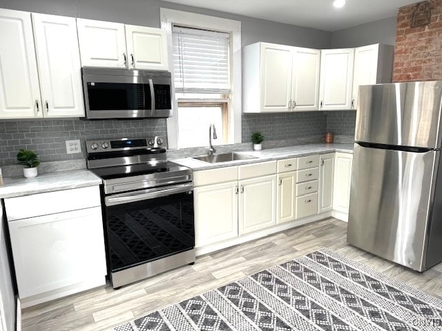 kitchen with sink, appliances with stainless steel finishes, white cabinets, light hardwood / wood-style floors, and backsplash