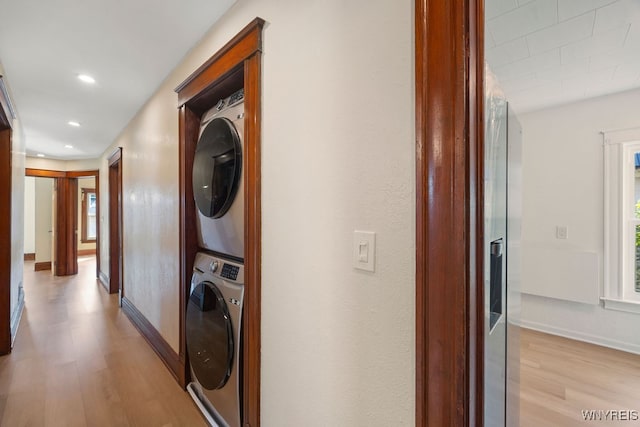 clothes washing area featuring stacked washer / drying machine and light hardwood / wood-style flooring