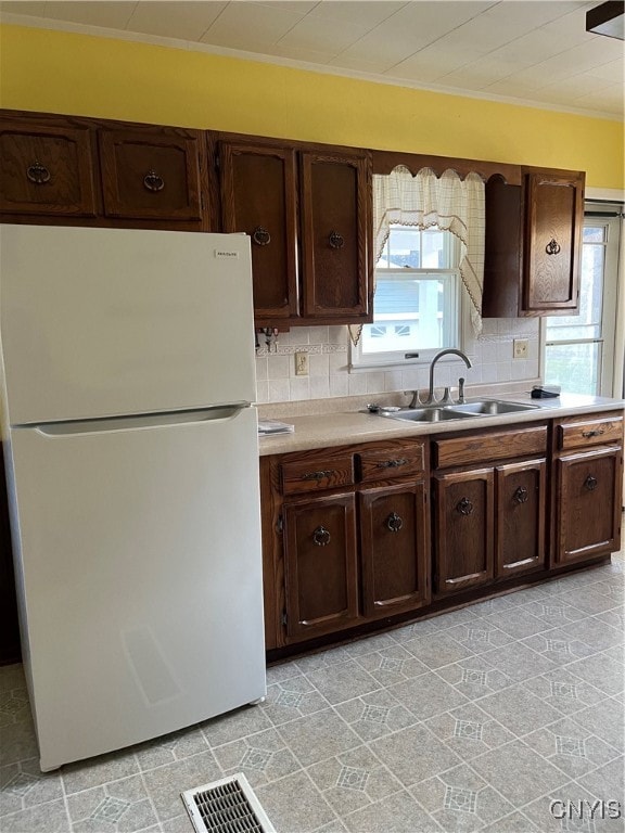 kitchen featuring sink, white refrigerator, backsplash, dark brown cabinets, and ornamental molding