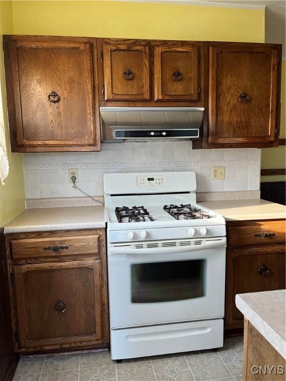 kitchen featuring white range with gas stovetop, range hood, and tasteful backsplash