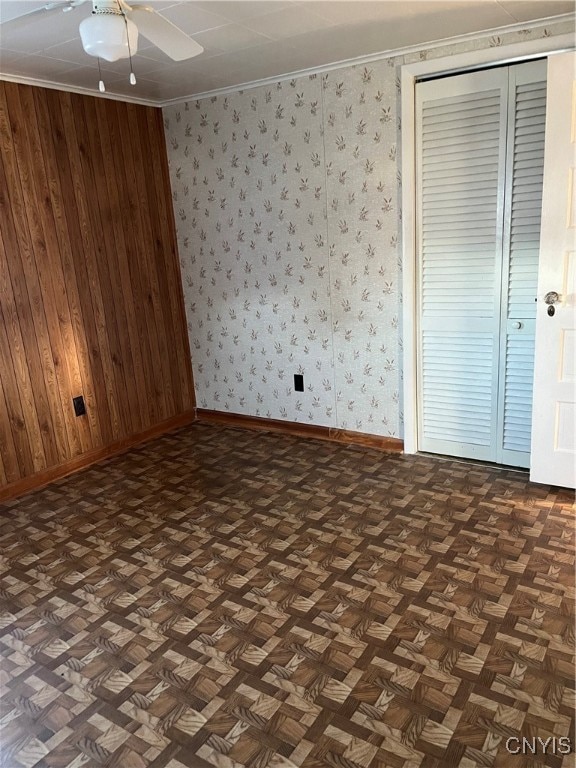 unfurnished bedroom featuring dark parquet flooring, crown molding, ceiling fan, and wooden walls