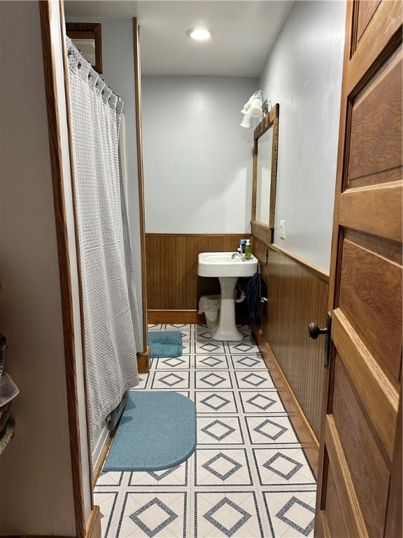 bathroom with a shower with shower curtain, wood walls, and sink