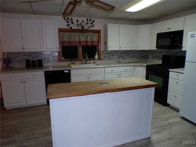 kitchen featuring sink, a kitchen island, light hardwood / wood-style floors, white cabinets, and black appliances