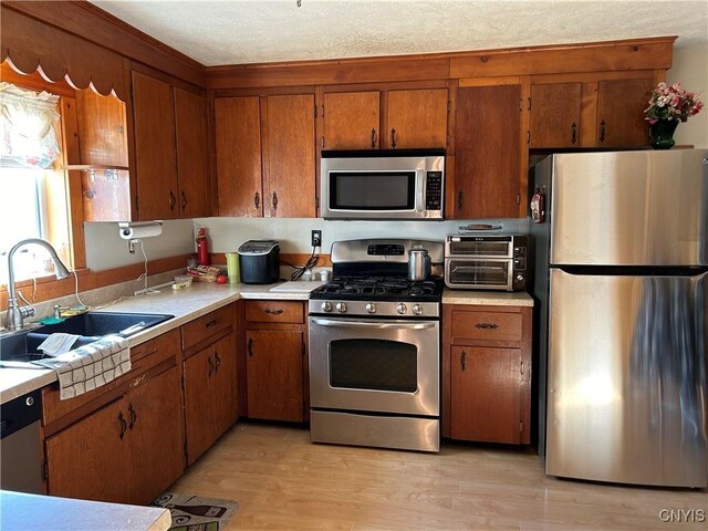 kitchen with sink, stainless steel appliances, a textured ceiling, and light hardwood / wood-style floors