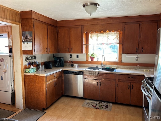 kitchen featuring appliances with stainless steel finishes, light wood-type flooring, a textured ceiling, sink, and washer / dryer