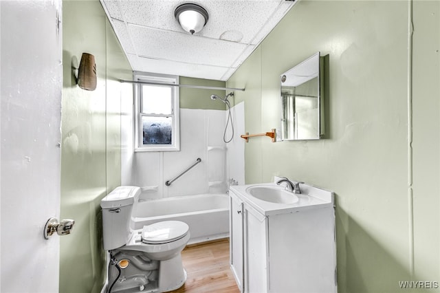 full bathroom featuring vanity, a drop ceiling, shower / washtub combination, hardwood / wood-style flooring, and toilet