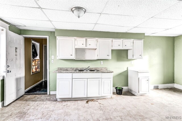 kitchen with a paneled ceiling, white cabinetry, and sink