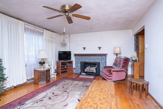 living room with hardwood / wood-style floors, a stone fireplace, and ceiling fan