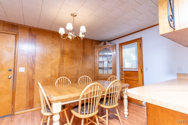 dining room featuring crown molding, wood walls, light hardwood / wood-style flooring, and a chandelier