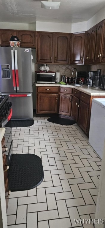 kitchen featuring stainless steel appliances, a sink, light countertops, dark brown cabinets, and decorative backsplash