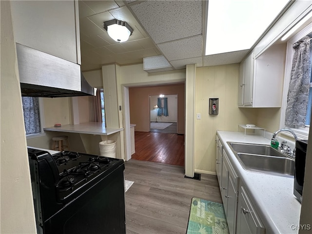 kitchen featuring white cabinetry, a drop ceiling, black stove, sink, and light hardwood / wood-style flooring