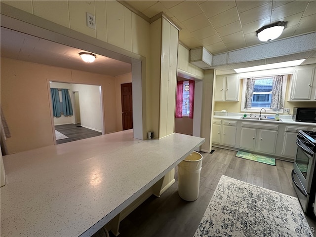 kitchen featuring stainless steel stove, light hardwood / wood-style flooring, white cabinetry, and sink