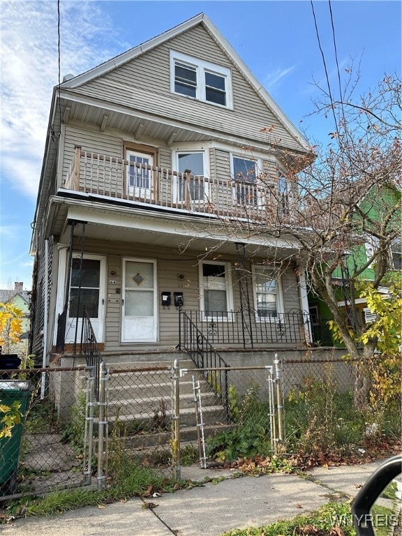 view of front of property with a balcony, a fenced front yard, a gate, and a porch