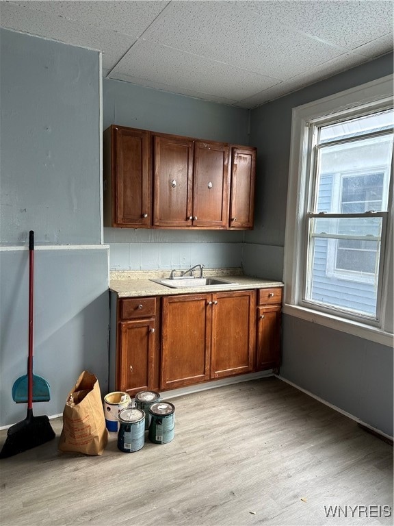 kitchen featuring brown cabinets, light wood finished floors, light countertops, a sink, and a drop ceiling